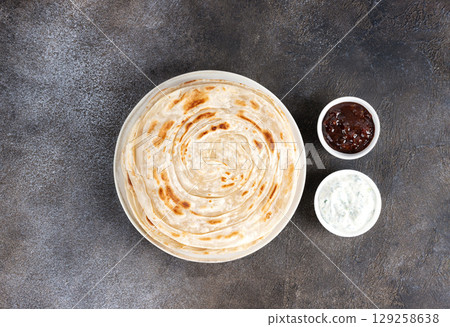 Indian flatbread paratha with raita sauce and chutney on gray background, top view. Indian food. Indian flatbread paratha with raita sauce and chutney on gray background, top view. Indian food. 129258638