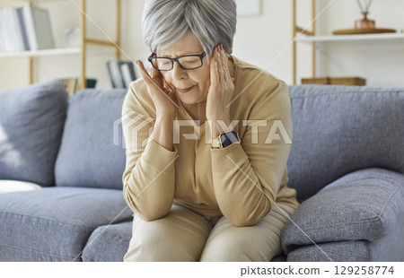 Tired frustrated old senior woman touching head, feeling headache, migraine, sitting on couch 129258774