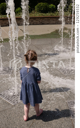 Little girl playing with water jets of a fountain in a leisure park 129259332