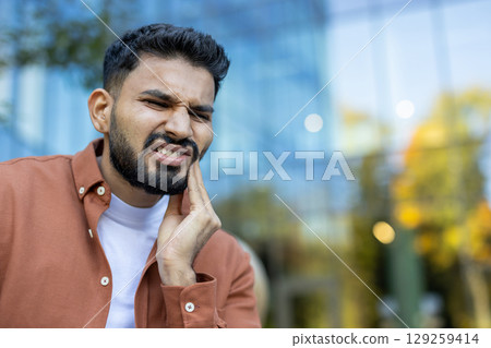 An Indian man is experiencing a painful toothache, expressing discomfort by touching his cheek. An Indian man is experiencing a painful toothache, expressing discomfort by touching his cheek. 129259414