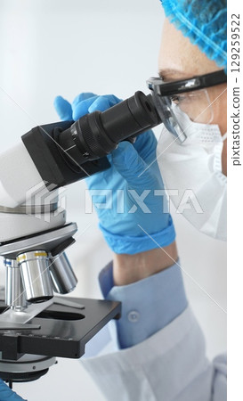 Female scientist in blue gloves and mask using microscope in laboratory setting, conducting important research and analysis, close-up. Medicine and science concept 129259522