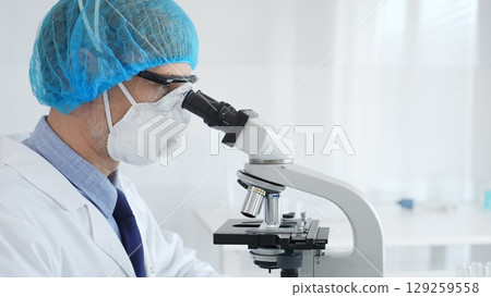 Experienced scientist examining microscopic sample, wearing full protective gear inside sterile research laboratory. Health care and science concept 129259558