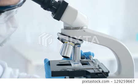 Close up of microscope and scientist's hands in blue gloves adjusting it in laboratory. Medicine, science concept Close up of microscope and scientist's hands in blue gloves adjusting it in laboratory. Medicine, science concept 129259667