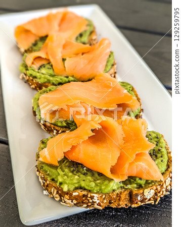 Delicious sandwich with salmon, avocado on plate, closeup Delicious sandwich with salmon, avocado on plate, closeup 129259795