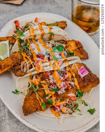 Close up of fresh white fish tacos with coleslaw, avocado, salsa and lime creme 129260054