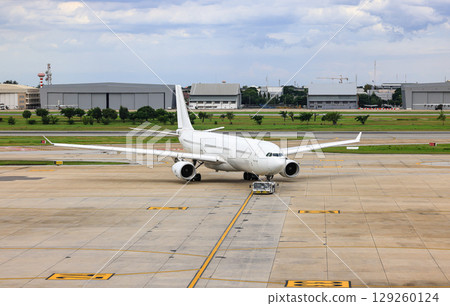 White commercial aircraft are pushed back to the taxiway by airplane tugs, with one in ground handling services White commercial aircraft are pushed back to the taxiway by airplane tugs, with one in ground handling services 129260124