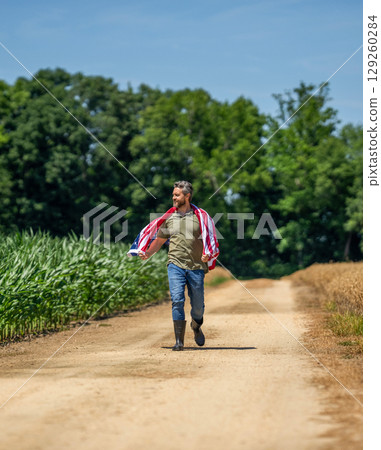 Man in field. Man with American flag in crop field. Independence day of America. 4th July. American labor day. American flag and man farmer. Flag of USA. Independence day. Patriotic symbol Man in field. Man with American flag in crop field. Independence day of America. 4th July. American labor day. American flag and man farmer. Flag of USA. Independence day. Patriotic symbol 129260284