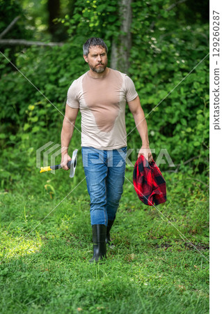 Strong man work in forest. Lumberjack men in forest with axe. Lumberjack carries axe. Deforestation. Handsome man with axe. Lumberjack in woods with an ax. Lumberjack in shirt with heavy axe 129260287
