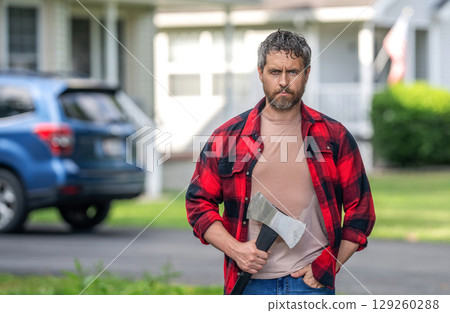 Sweating man with axe. Lumberjack at backyard with an ax. Lumberjack with heavy axe. Strong sweating man after hard work. Lumberjack man with axe, copy space. Lumberjack carries axe 129260288