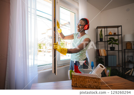 Smiling housekeeper opening window while listening to music with headphones 129260294