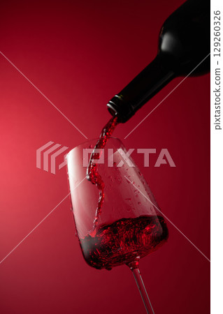 Pouring red wine from a bottle into a glass. 129260326