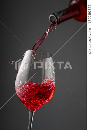 Pouring pink wine from a bottle into a glass. Pouring pink wine from a bottle into a glass. 129260331