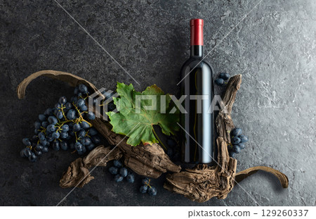 Bottle of red wine, blue grapes, and old vine snags on a black stone background. Bottle of red wine, blue grapes, and old vine snags on a black stone background. 129260337