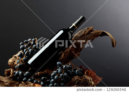 Bottle of red wine with blue grapes on old wooden snags. 129260348