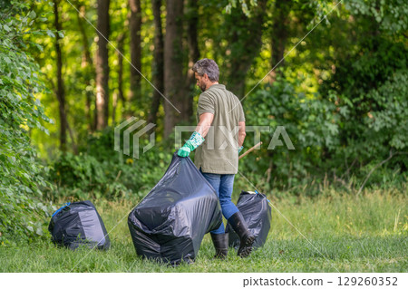 Ecology concept. Volunteer collecting garbage, ecology. Man in rubber gloves with trash bag clean garbage. Man collecting plastic trash. Eco volunteer. Garbage collecting in forest. Waste management 129260352