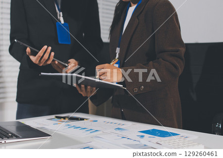 Focused young businessman signing agreement with skilled lawyer in eyeglasses. Concentrated financial advisor showing place for signature on paper contract document to male client at meeting in office Focused young businessman signing agreement with skilled lawyer in eyeglasses. Concentrated financial advisor showing place for signature on paper contract document to male client at meeting in office 129260461