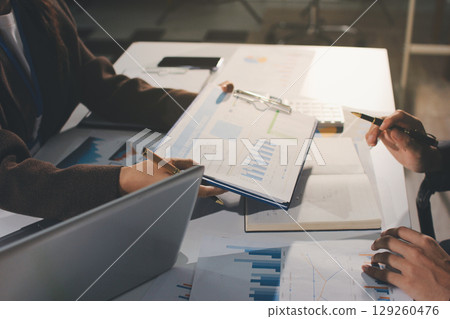 Focused young businessman signing agreement with skilled lawyer in eyeglasses. Concentrated financial advisor showing place for signature on paper contract document to male client at meeting in office Focused young businessman signing agreement with skilled lawyer in eyeglasses. Concentrated financial advisor showing place for signature on paper contract document to male client at meeting in office 129260476