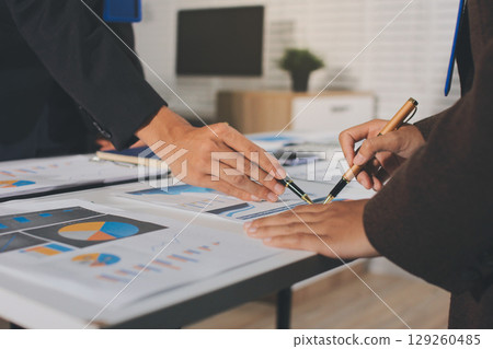 Focused young businessman signing agreement with skilled lawyer in eyeglasses. Concentrated financial advisor showing place for signature on paper contract document to male client at meeting in office Focused young businessman signing agreement with skilled lawyer in eyeglasses. Concentrated financial advisor showing place for signature on paper contract document to male client at meeting in office 129260485