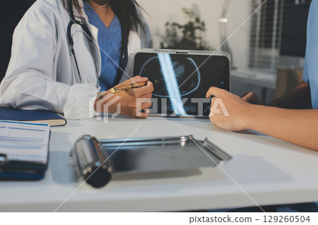 Cropped shot of an unrecognisable doctor sitting with his patient and showing her x-rays on a digital tablet 129260504