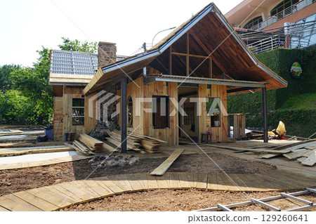 Wooden House Under Construction with Stone Chimney and Sloped Roof in a Scenic Green Hillside Area 129260641