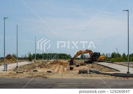 Excavator working at road construction site with light poles and curbs during infrastructure upgrade Excavator working at road construction site with light poles and curbs during infrastructure upgrade 129260647