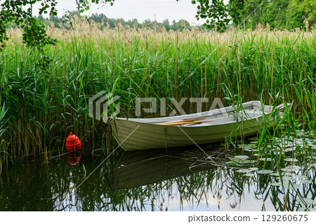 Rowboat Moored in Reeds on Calm Lake with Reflections and Red Buoy in Peaceful Nature Landscape 129260675