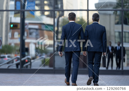 Walking colleague. Colleague and friends. Two successful business men walking outdoor. Businessmen go to work. Business talking. Two millennial businessmen in elegant business suit Walking colleague. Colleague and friends. Two successful business men walking outdoor. Businessmen go to work. Business talking. Two millennial businessmen in elegant business suit 129260766