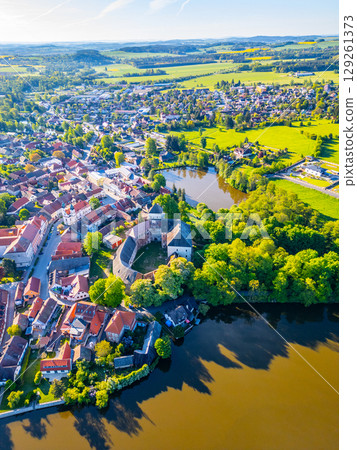 Overlooking Rozmital pod Tremsinem, this aerial view captures the charming town, ancient castle, and surrounding lush greenery reflecting on the serene waters below, showcasing a peaceful landscape. Overlooking Rozmital pod Tremsinem, this aerial view captures the charming town, ancient castle, and surrounding lush greenery reflecting on the serene waters below, showcasing a peaceful landscape. 129261373