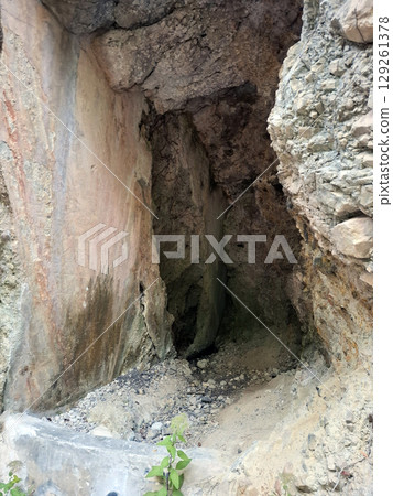 The cave entrance showcases rugged stone walls with shades of brown and gray. Surrounding vegetation hints at the remote location of this intriguing natural feature. 129261378