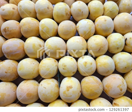 Yellow plums are arranged neatly, highlighting their smooth skin and vivid color. This display captures the freshness and appeal of seasonal fruit typical in local markets. 129261397