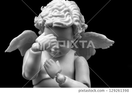 Sad cherub with facepalm gesturing. Angel figurine holding his head in hands on black background 129261398