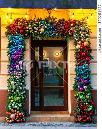 Wooden door decorated with multicolored Christmas baubles Wooden door decorated with multicolored Christmas baubles 129261422
