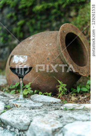 Glass of Red Wine with Traditional Georgian Qvevri in Rustic Setting 129261538