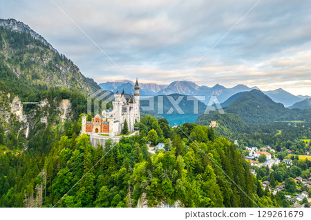 Neuschwanstein Castle rises dramatically over lush green forests and mountains in Bavaria, Germany. This fairytale chateau captivates visitors with its enchanting architecture and scenic surroundings. 129261679