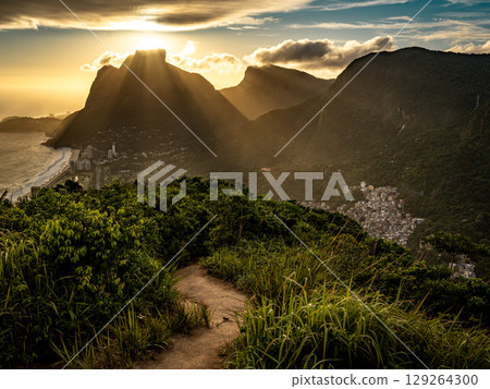 Golden Sunset Over Rio De Janeiro From Two Brothers Mountain: Dramatic Sunbeams Streaming Through Coastal Peaks Above The Atlantic Ocean And Leblon Beach 129264300