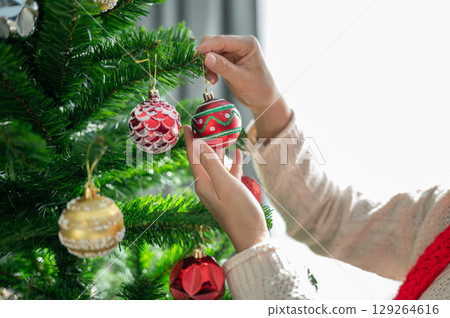 Cropped shot view of woman hands decorating Christmas tree during Christmas festival and New Year celebration. 129264616