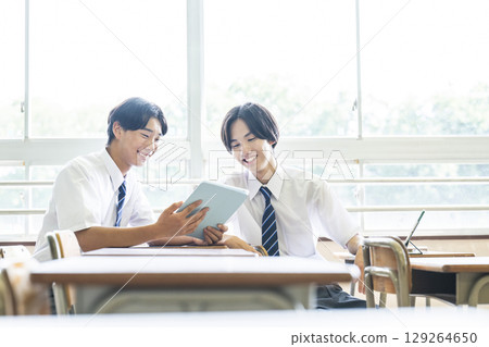A male junior high school student looking at a tablet with friends A male junior high school student looking at a tablet with friends 129264650