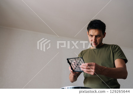 Portrait of technician male carefully inspecting and cleaning air humidifier filter, ensuring clean and healthy air in home environment, performing regular maintenance for optimal performance. Portrait of technician male carefully inspecting and cleaning air humidifier filter, ensuring clean and healthy air in home environment, performing regular maintenance for optimal performance. 129265644