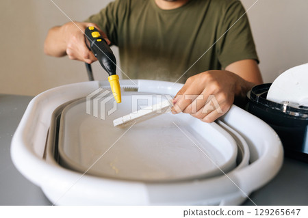 Person using steam cleaner for sanitizing humidifier filter submerged in basin of water, promoting clean and healthy air for improved indoor air quality and wellness. Concept of hygiene, cleanliness. Person using steam cleaner for sanitizing humidifier filter submerged in basin of water, promoting clean and healthy air for improved indoor air quality and wellness. Concept of hygiene, cleanliness. 129265647