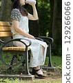 A young woman sitting on a bench in the shade of a tree and drinking water from her own bottle 129266066