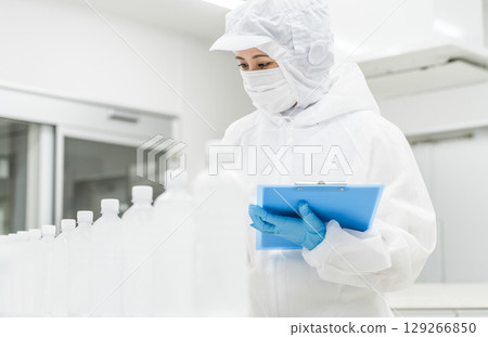 A production staff member in a dustproof suit checking bottled water at a water factory and beverage manufacturer (beverage manufacturer) 129266850