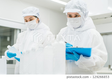 A production staff member in a dustproof suit checking bottled water at a water factory and beverage manufacturer (beverage manufacturer) 129266853