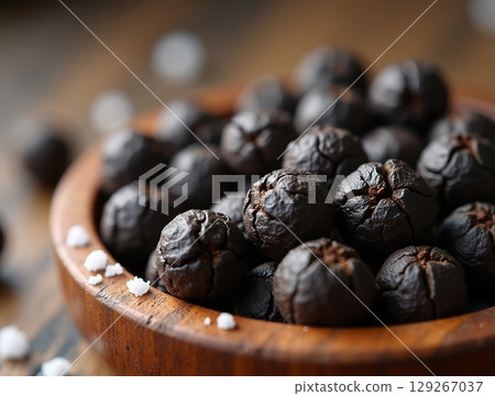 Macro Close-up of Black Peppercorns and Salt Crystals in a Wooden Bowl 129267037
