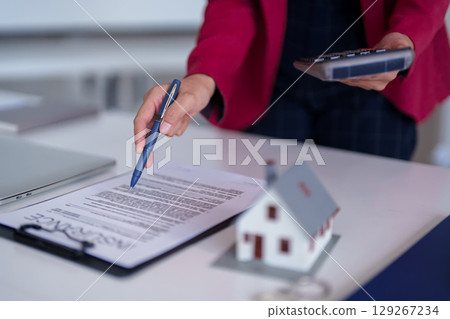 Adult professional hand pointing to home insurance contract with calculator and miniature house on desk for property sale Adult professional hand pointing to home insurance contract with calculator and miniature house on desk for property sale 129267234