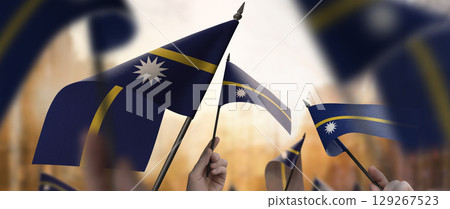 Nauru flags in their hands on a blurred urban background 129267523