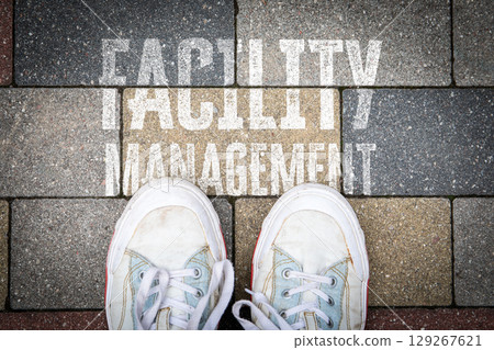 Facility Management Concept with Shoes on Pavement and Text on Colored Brick Background Facility Management Concept with Shoes on Pavement and Text on Colored Brick Background 129267621