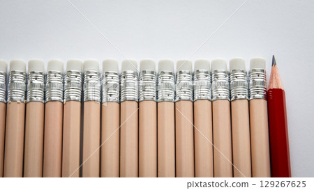 Standing Out from the Crowd. One Red Pencil Among Identical Erasers 129267625