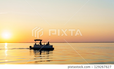 Silhouette of Pontoon Boat Sailing on Calm Water at Sunset, A Serene Evening Excursion 129267827