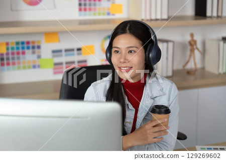 Creative Workspace. Young woman smiling while holding coffee and working on a computer. Creative Workspace. Young woman smiling while holding coffee and working on a computer. 129269602