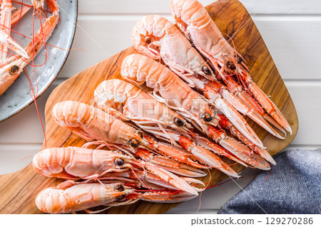 Scampi langoustine on cutting board on white table. Top view. Scampi langoustine on cutting board on white table. Top view. 129270286